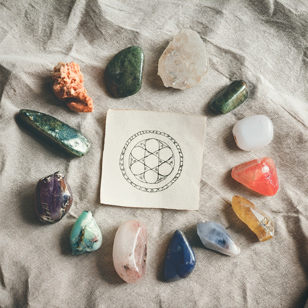 Collection of zodiac birthstones arranged with chakra symbols on fabric.