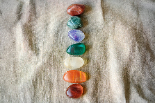Seven chakra crystals arranged in order of chakra colors on linen.