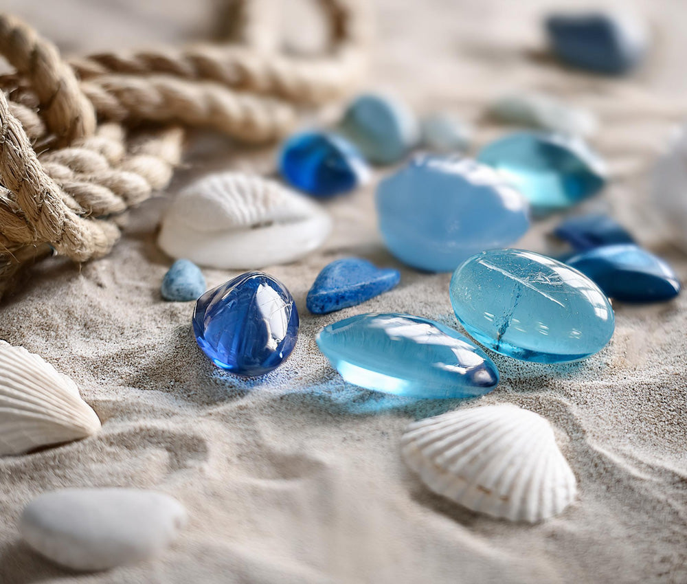 Aquamarine gemstones displayed on a sandy-textured surface, showcasing their serene blue tones and subtle nautical connections.