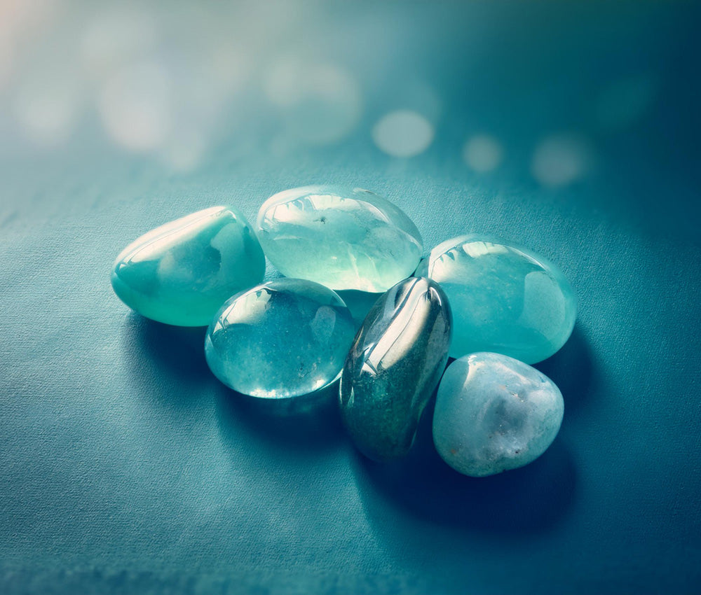 Aquamarine stones on a smooth surface with soft blue lighting, emphasizing their connection to the Throat and Heart Chakras.