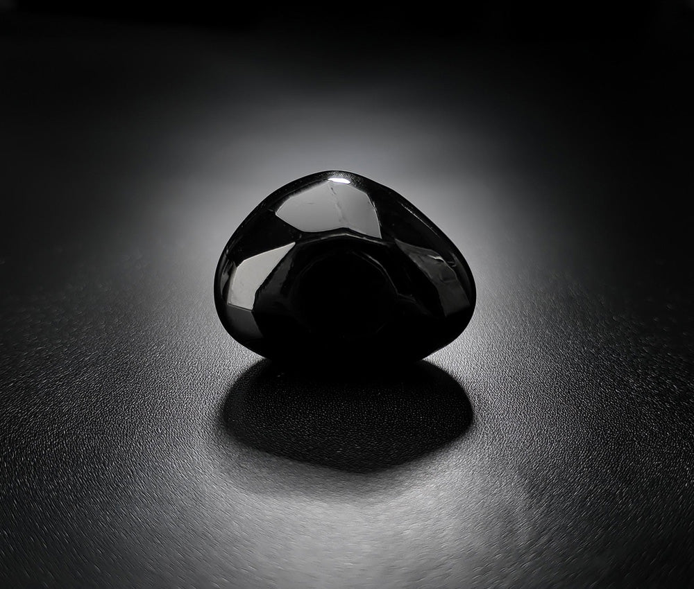 Polished obsidian stones on a dark surface, symbolizing their historical use in tools, ceremonies, and spiritual practices.